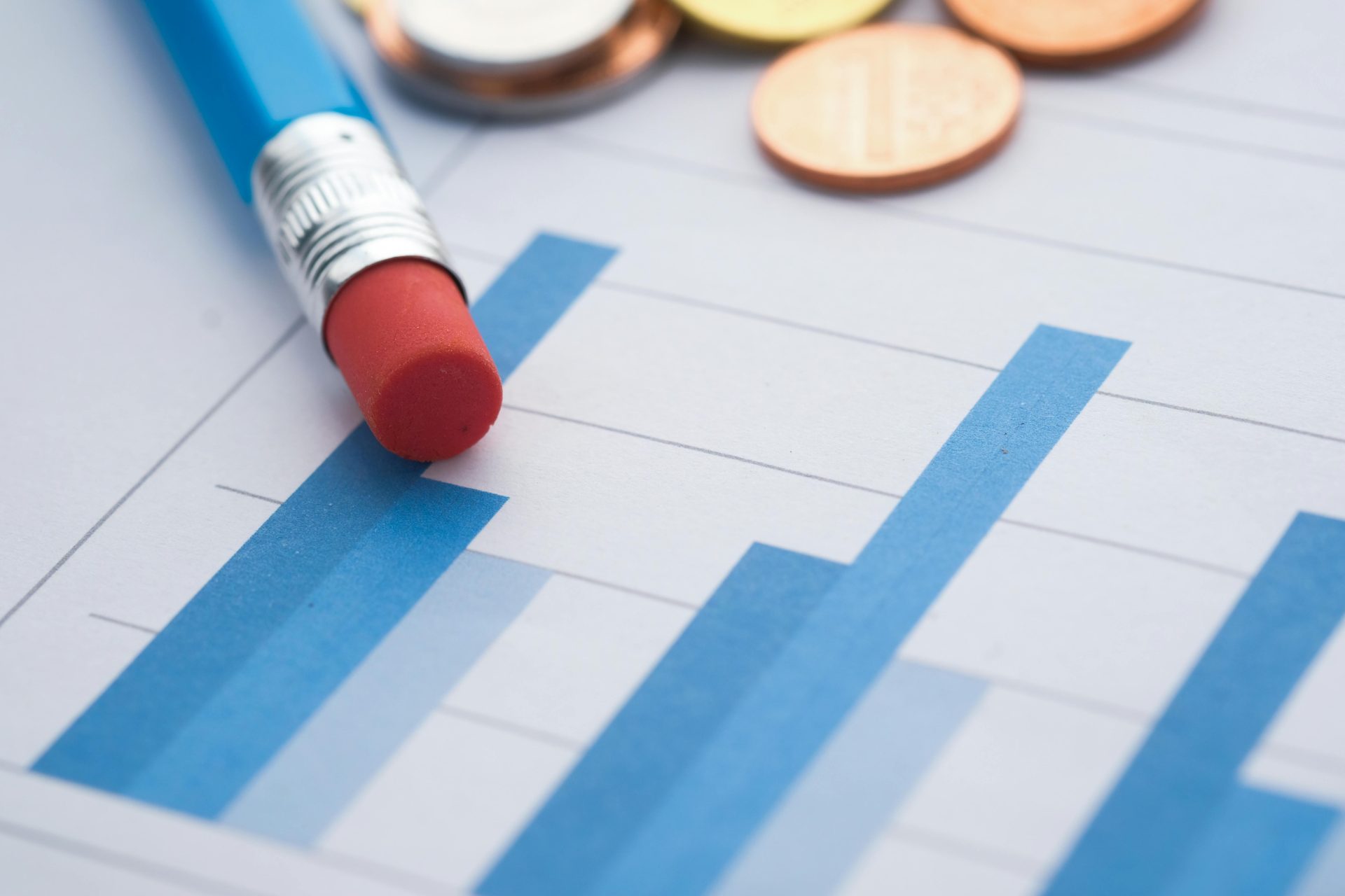 Nahaufnahme von Balkendiagrammen mit einem Bleistift und Münzen, die eine Finanzanalyse symbolisieren.