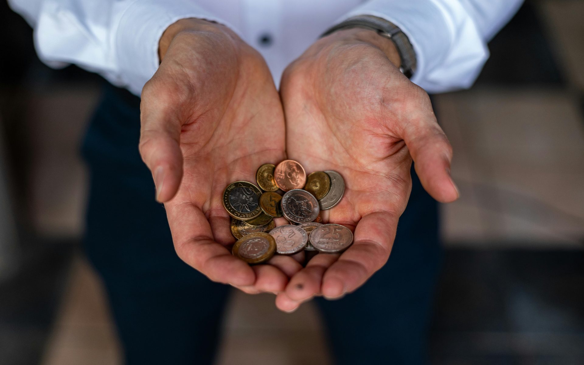 Nahaufnahme von Händen, die verschiedene argentinische Peso-Münzen halten – ein Symbol für Währung und Finanzen in Argentinien.