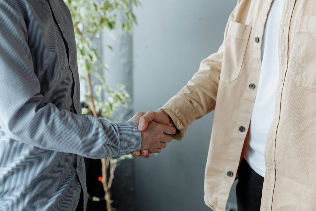 Eine Nahaufnahme zweier Geschäftsleute, die sich in einer Büroumgebung die Hand geben – ein Symbol für Einigung und Partnerschaft.