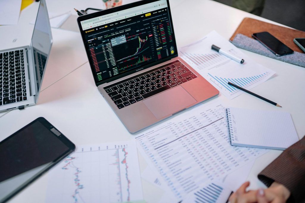 Laptops auf einem Schreibtisch, die Börsencharts und Finanzdokumente anzeigen.