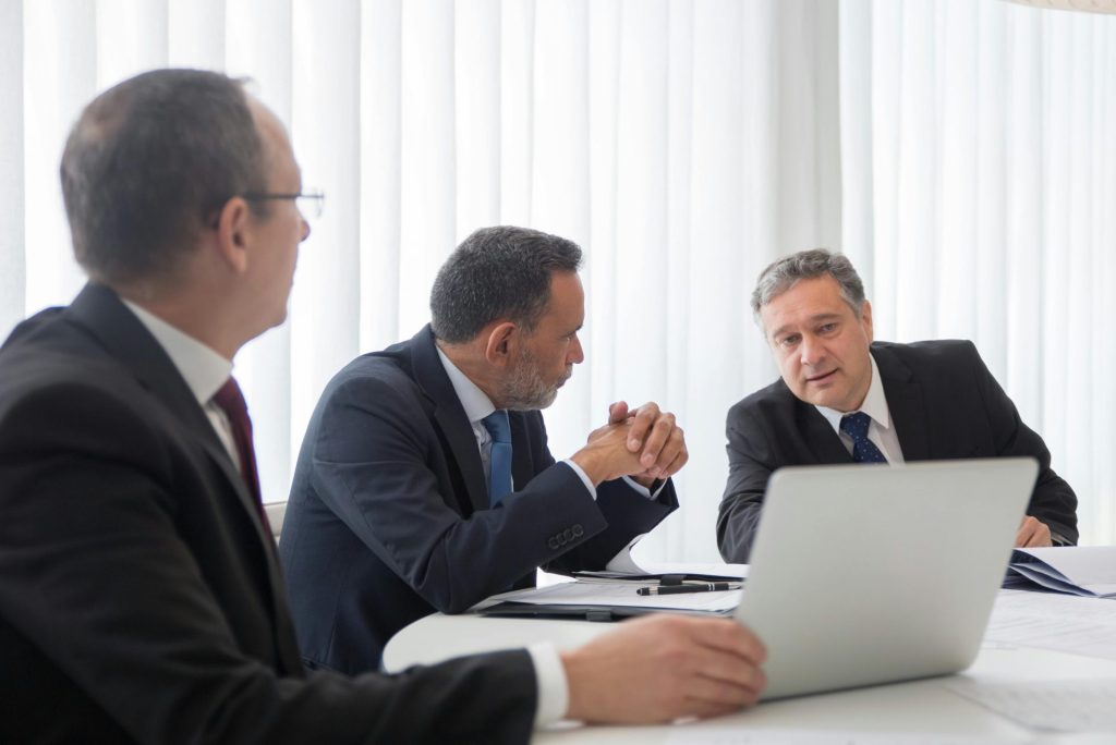 Drei Geschäftsleute arbeiten während eines Meetings an einem Laptop in einem hellen Büro zusammen.